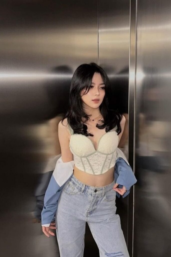 Young woman in a light green corset top and light blue jeans.