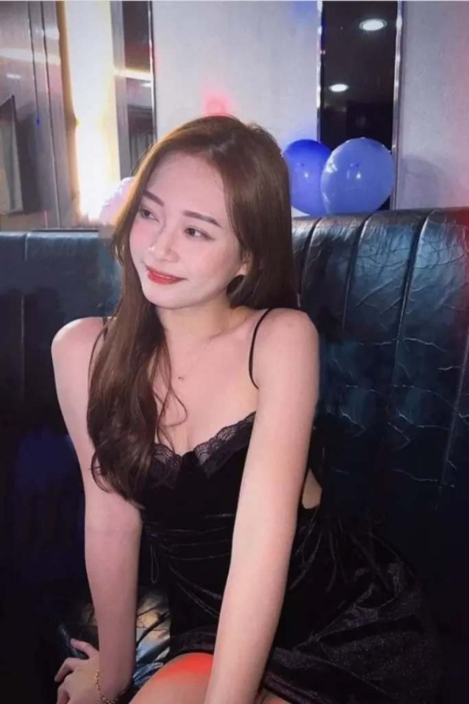 Young woman in a black velvet dress, posing on a couch.