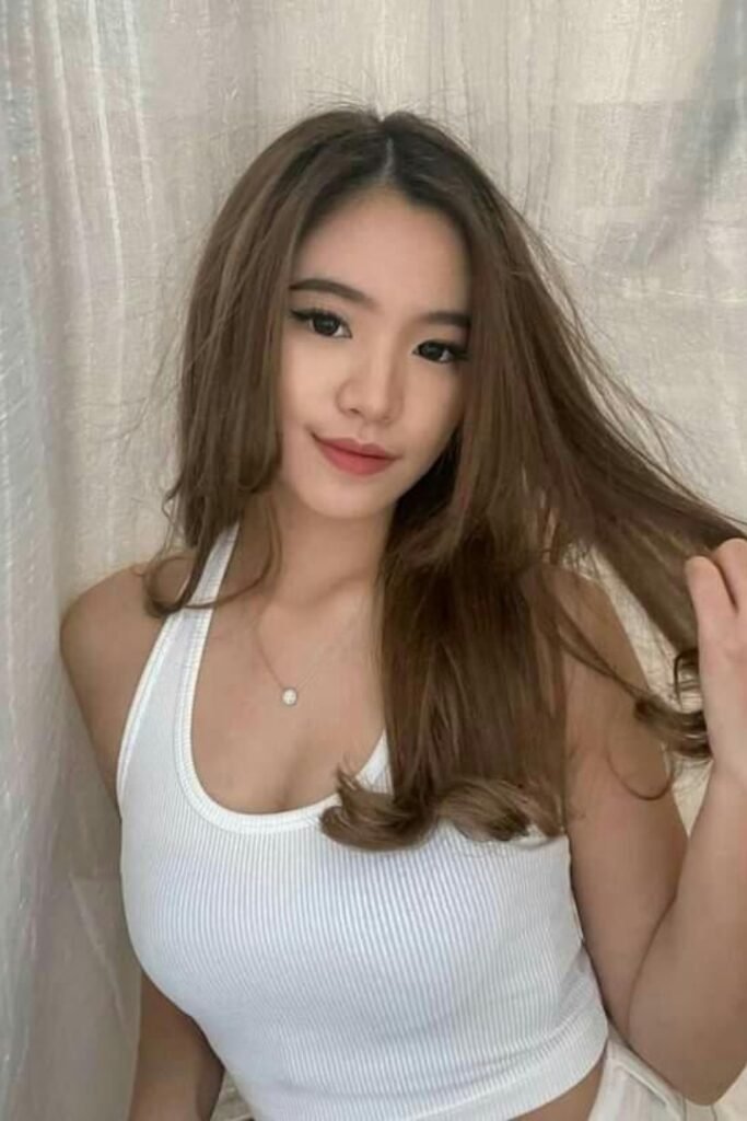 Young woman with long brown hair, wearing a white ribbed tank top.
