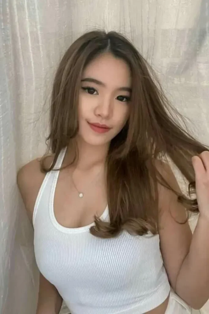 Young woman with long brown hair wearing a white ribbed tank top.