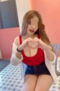 Woman in red top and denim shorts making a heart shape with her hands