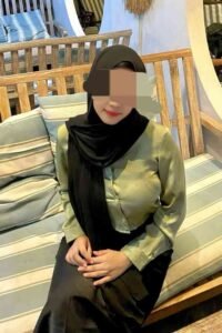 Woman in hijab and green blouse sitting on a bench.