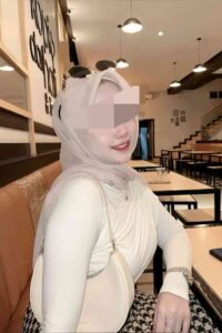 Woman in hijab at cafe, wearing cream top and patterned skirt.