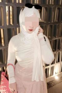 Woman in hijab, sunglasses, and pink skirt, holding a pink purse.